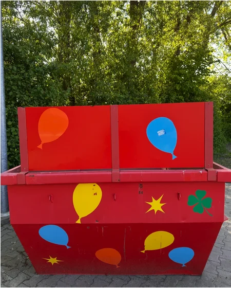 Rote Poltermulde mit bunten Luftballons und Kleeblatt in der Frontansicht